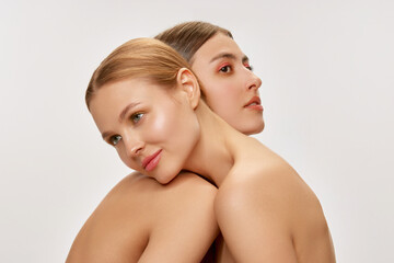 Closeup portrait of two adorable young girls with well-kept skin posing over grey background. Models with bare shoulders. Concept of beauty, spa, skin care and health