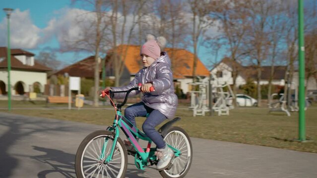 Slow motion: child rides bicycle in park. Kid learning to ride bike. Happy girl traveling by bike in spring. Happy childhood, sports outdoors in playground