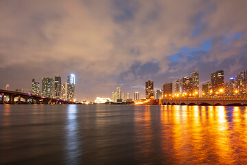 Obraz premium View of Miami at sunset, USA. Miami city skyline panorama at dusk with urban skyscrapers and bridge over sea with reflection.