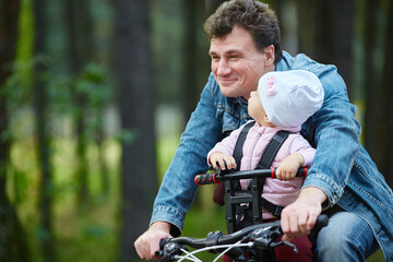 Dad and a small child ride a bicycle in the summer through the forest using a bicycle chair for children.
