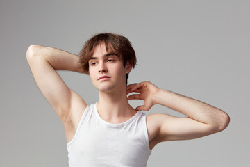 Studio portrait of young man with well-kept skin posing in singlet against grey background. Concept of men's health, body and skin care, hygiene and male cosmetology