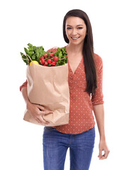 A happy female model with a smiling face following a vegetables diet and holding a shopping bag filled with nutritious healthy and organic groceries and food items isolated on a PNG background.