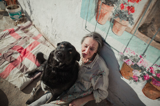 Mature woman sitting on the floor of her terrace sunbathing with her dog
