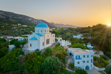 Naklejka premium Aerial view of the Lagoudi Zia Church on Greek island of Kos. Typical blue roofs monastery near Zia town against Sunset. Vibrant colors, no people, calm atmosphere.