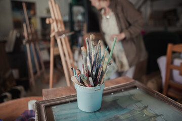 Close-up of paint-stained brushes, in the out-of-focus background a woman paints a picture