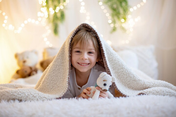 Little cute preschool boy, holding cute teddy bear, hiding under blanketl, playing at home in bedroom