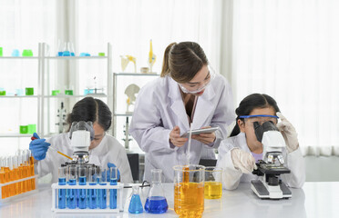 woman scientist as a mentor is teaching the students asian children in scientist uniform trying to...