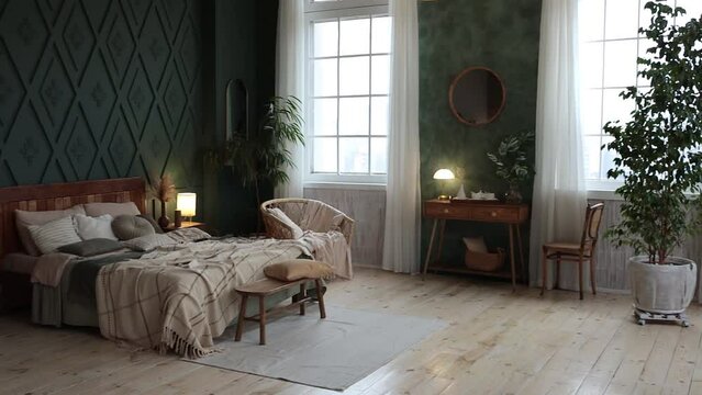 Cozy bedroom interior in boho style with emerald walls, wooden furniture, console table, textiles, large windows and potted plants. Empty space