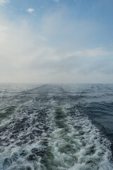 Wake of vessel. Wide wake trail from boat. Ocean water. Deep blue. Trace from large ship. Sunset rays on water from luxury sail yacht. Ship Sailing on Sea. Waves from the back of speed boat over the