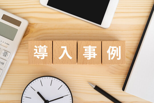 導入事例と書かれたブロック、電卓、スマホ、時計、ノート

