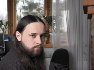 Portrait of a young handsome concentrated pensive man with a black beard posing for the camera. Life, life, modern technologies and hobbies of youth.