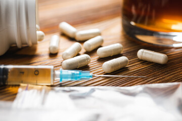 White pills, syringe with a drugs dose, narcotics, glass with alcohol drink on a wooden table, close-up view. Concept of addiction and bad habits