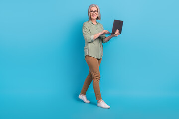 Full body length photo cadre of successful business woman walking with laptop freelancer online communication isolated on blue color background