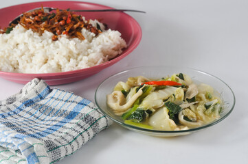 mustard greens and mushrooms are served on a small plate, white rice with anchovy and a napkin isolated on a white background