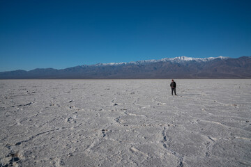 An older woman is standing in Badwater Basin. High quality photo showing the huge landscape with a single person for scale. 