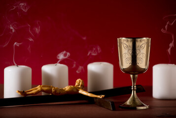 golden chalice with crucifix and extinguished candles with smoke red background