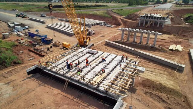 Construction team in hard hats work at the construction site aerial view. Concrete structure. Builders in the process of work. Construction Crane. Construction of a road bridge