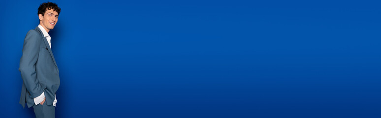 Smiling man in suit and shirt posing on blue background with copy space, banner.