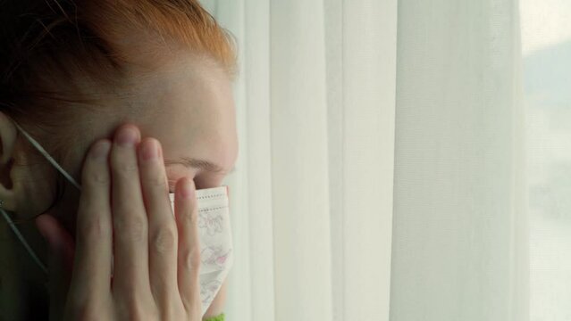 The girl in the mask is sick and longingly looks out the window into the street. Flu and fever.