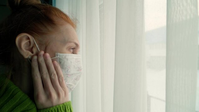 The girl in the mask is sick and longingly looks out the window into the street. Flu and fever.