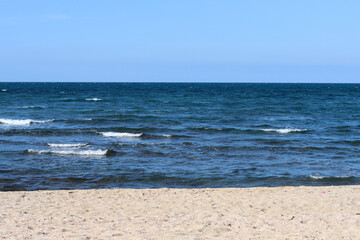 Sunny spring day on a beach. Calm sea water, blue sky, sandy beach. 