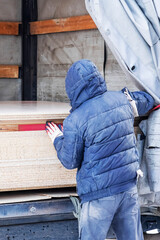 The average adult worker unloads chipboard from a truck.vertical