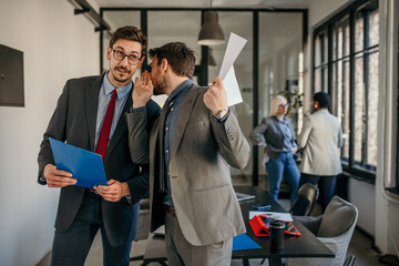 Shot of two coworkers gossiping and having a discussion in a modern office. Businessmen in meeting...