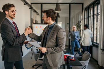 Shot of two coworkers handshaking and closing a deal in a modern office. Businessmen handshake after they check the paperwork and discuss business strategy. Confident business people working together