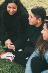 three people of hispanic-latino ethnicity sitting on the green grass of a park, with smart device