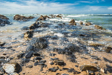 Black and wet rocks by the Atlantic Ocean and sand at Almograve beach in Costa Vicentina, PORTUGAL
