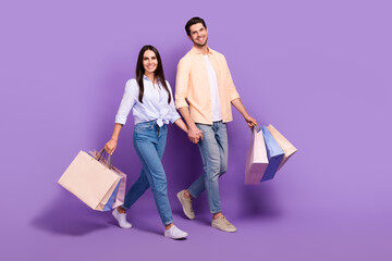 Full length photo of two cheerful lovely partners walk shopping hold arms isolated on violet color...