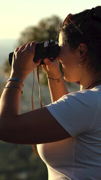 Young latin woman using binoculars in the mountain at sunset