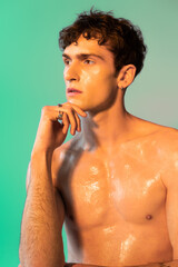 Shirtless man with oil on body looking away on green background.