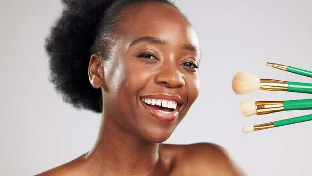 Face, makeup and smile of black woman with brushes in studio isolated on a gray background. Portrait, cosmetics and happy female model laughing with tools to apply foundation or powder for beauty.