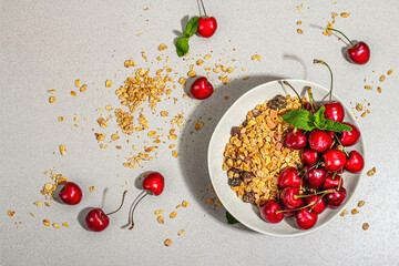 Summer breakfast concept. Healthy morning food. Ripe cherries and granola, light concrete background