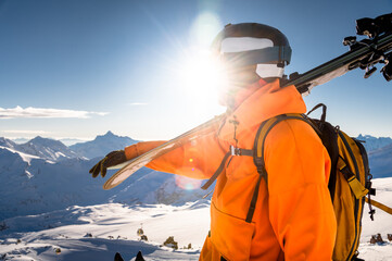 Portrait of a man holding skis on his shoulder and looking at a snowy mountain against the backdrop...