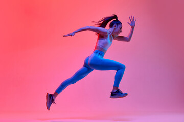 Fototapeta na wymiar Dynamic portrait of young active girl, athlete, runner in motion, training over pink studio background in neon light. Concept of sportive lifestyle, health, endurance, action and motion. Ad