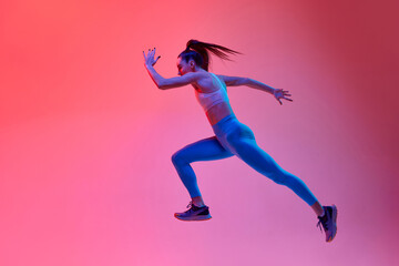 Fototapeta na wymiar Dynamic portrait of young active girl, running athlete in motion, training over pink studio background in neon light. Concept of sportive lifestyle, health, endurance, action and motion. Ad