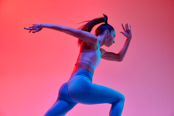 Speed. Dynamic image of young active girl, athlete, runner in motion, training over pink studio background in neon light. Concept of sportive lifestyle, health, endurance, action and motion. Ad
