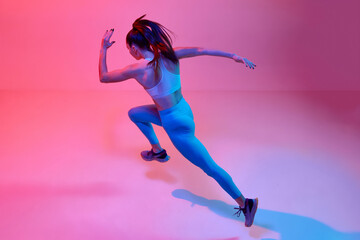 Top view dynamic image of professional female runner, athlete training over pink studio background in neon light. Concept of sportive lifestyle, health, endurance, action and motion. Ad