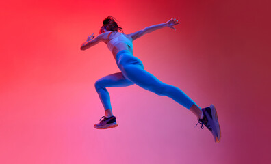 Fototapeta na wymiar Bottom view. Young female professional athlete, runner in motion, training over pink studio background in neon light. Concept of sportive lifestyle, health, endurance, action and motion. Ad