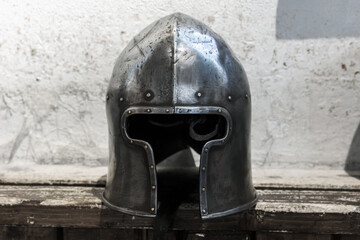 Steel helmet of medieval knight lays on a rough wooden shelf
