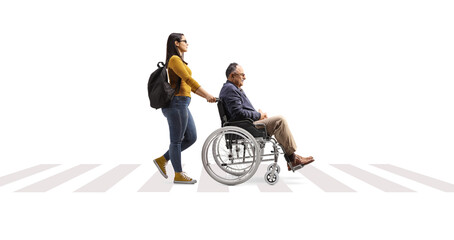 Full length profile shot of a young woman pushing a mature man in a wheelchair on a pedestrian crossing