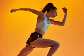 Speed up. Young girl, professional runner athlete in uniform training, running over orange studio...