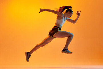 Speed. Dynamic image of young girl, professional athlete, runner in motion, training on orange...