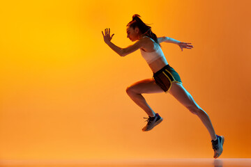 Fototapeta na wymiar Dynamic image of professional female runner, athlete in motion, running over orange studio background in neon light. Concept of sportive lifestyle, health, competition, endurance, action. Ad