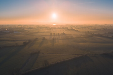 Fototapeta na wymiar Sunrise over Schleswig-Holstein, Germany with klong shadows of trees, fog and morning dew