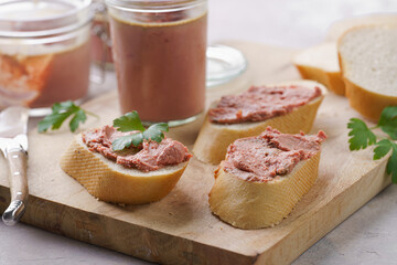 Homemade chicken liver pate on fresh french white wheat baguette slices on wooden plate, glass mason jars with cooked liverwurst, top view