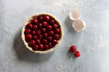Homemade sweet cherry pie in a making. Close up photo of fruit tart on light grey table. 