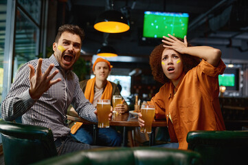 Cheering friends of soccer fans with creative makeup in faces in pub